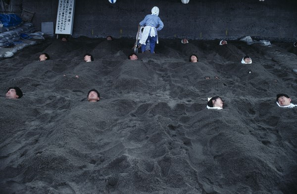 JAPAN, Kyushu, Ibusuki, Hot Sand Bath. People submerged in sand with their heads pocking out above the surface.