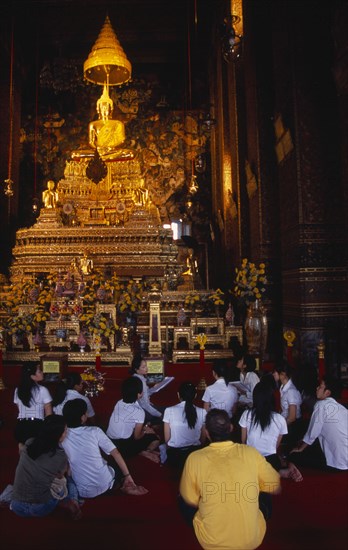 THAILAND, South, Bangkok, Wat Pho main prayer hall with a group of Thai students and teacher seated in front of Golden seated Buddha