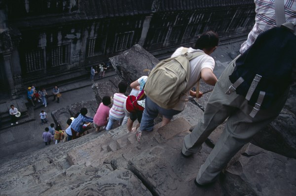 CAMBODIA, Siem Reap Province, Angkor Wat, Line of tourists climbing down steep and narrow steps of tower in upper level.