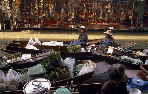 THAILAND, South, Bangkok, Damnoen Saduak Floating Market fruit vendors in their canoes with a tourist goods stall on the far bank of the canal