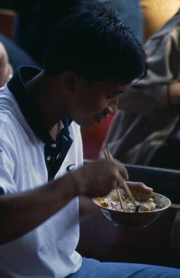 THAILAND, South, Bangkok, Damnoen Saduak Floating Market man sitting in a canoe eating noodles