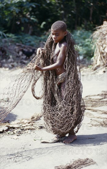 CONGO, The Ituri Forest, Pygmy boy sorting fishing nets on sand for hunting trip.