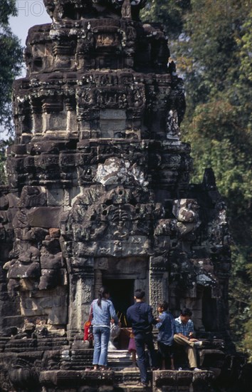 CAMBODIA, Siem Reap Province, Angkor, Neak Pean.  Tourists lighting incense at entrance to small temple on circular terrace.