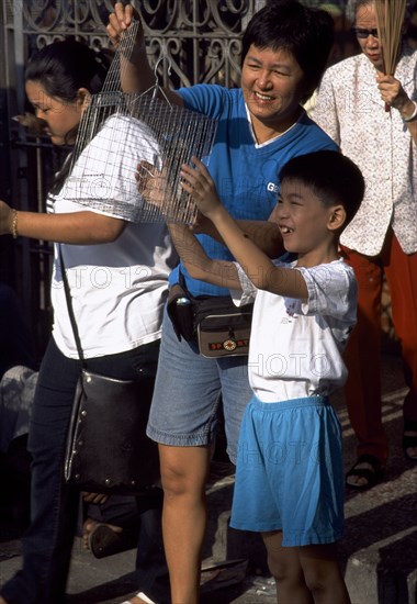 MALAYSIA, Penang, Georgetown, Kuan Yin Teng or Temple of Mercy with young boy releasing a caged bird to earn merit