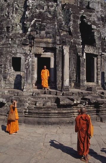 CAMBODIA, Siem Reap, Angkor Thom, Bayon Temple with three monks taking photographs of each other on the top level