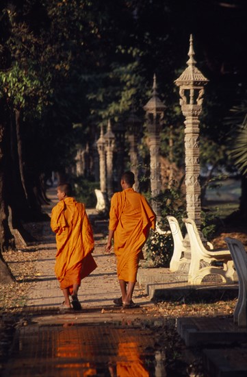 CAMBODIA, Siem Reap, Siem Reap Town, Two monks walking along the path lined with stone lanterns through the trees by the river