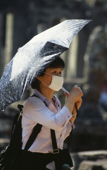 CAMBODIA, Siem Reap Province, Angkor Thom, Japanese tourist at Bayon Temple wearing a face mask and holding an umbrella for shade