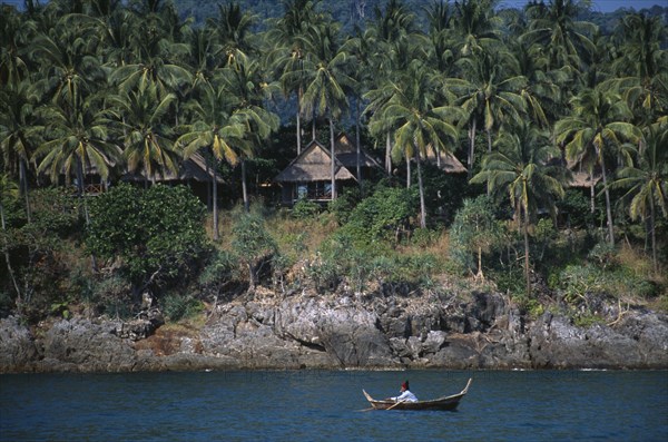 THAILAND, Krabi, Koh Lanta Yai, The Narima Spa Resort chalets amongst coconut palm trees with a man on a small fishing boat offshore
