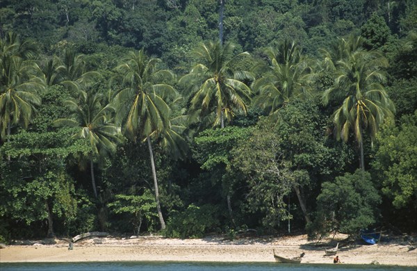 THAILAND, Krabi, Koh Lanta Marine NP, Koh Rok with a man beside a fishing boat on the shoreline below the tree lined hill