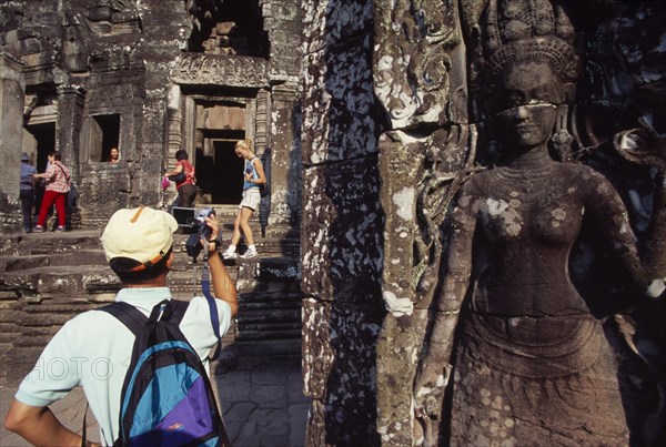 CAMBODIA, Siem Reap Province, Angkor Thom, The Bayon.  Tourists with cameras and videos with bas relief carving of apsara in the foreground.