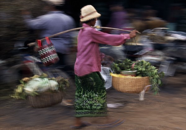 CAMBODIA, Siem Reap, Woman carrying fresh produce in two baskets balanced on a pole over her shoulder