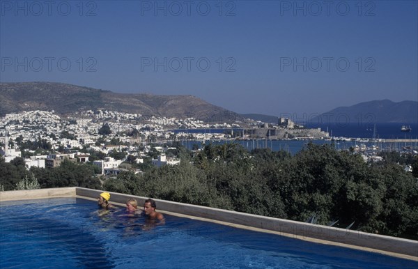 TURKEY, Aegean Region, Mugla, Bodrum.  People in swimming pool of Antik Theatre Hotel in foreground with view over resort to fifteenth century castle of St Peter beyond.