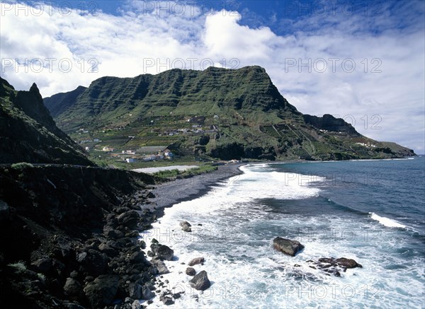 SPAIN, Canary Islands, La Gomera, Hermigua.  Coastal landscape with narrow beach of black volcanic sand and village houses on steep terraced hillside.