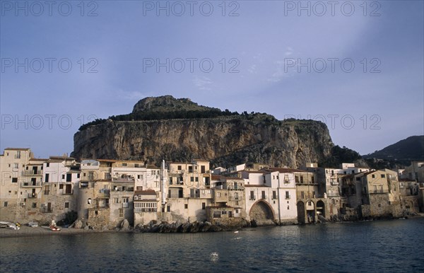 ITALY, Sicily, Cefalu, Town houses on edge of water with huge rock behind once the site of a Temple of Diana.