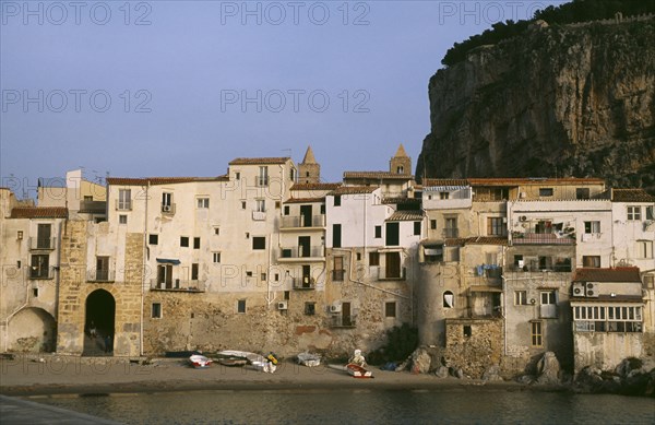 ITALY, Sicily, Cefalu, Town houses on edge of water with huge rock behind once the site of a Temple of Diana.