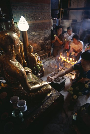 THAILAND, South, Bangkok, Wat Pho small shrine beside the reclining Buddha with devotees making offerings to small Golden Buddhas