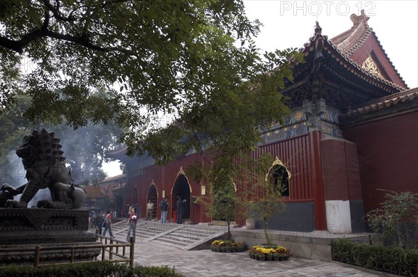 CHINA, Beijing, Lama Temple. People looking around the buildings of the Temple complex with stone lion statue in the foreground