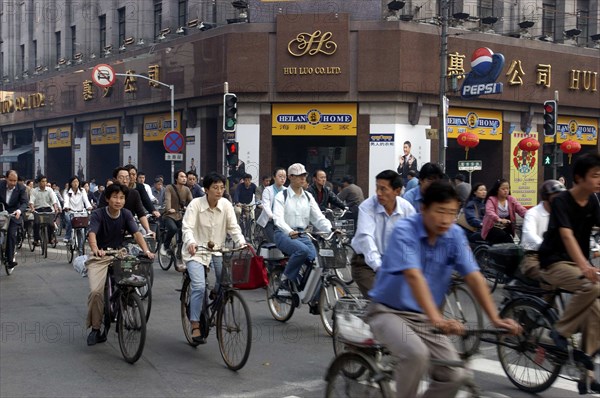 CHINA, Shanghai, Mass of cyclists passing a crossroads at the traffic lights outside the Hui Luo Co. Ltd building