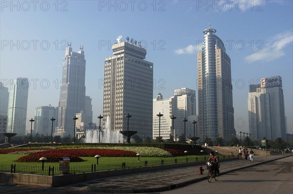 CHINA, Shanghai, Modern city skyline with flowerbeds and fountain in the foreground with passing cyclist