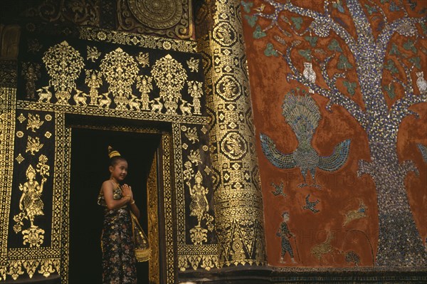 LAOS, Louangphrabang , Young girl dressed for Lao New Year at Wat Xieng Thong with highly decorated exterior.