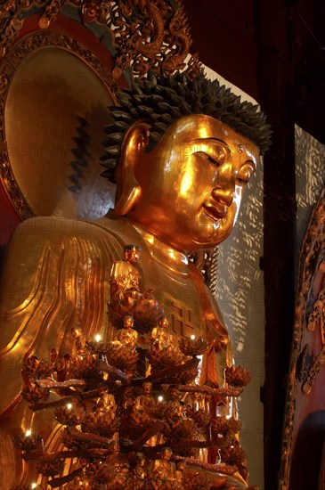 CHINA, Shanghai, Jade Buddha Temple. Golden Buddha statue with seated Buddha candle stand in front