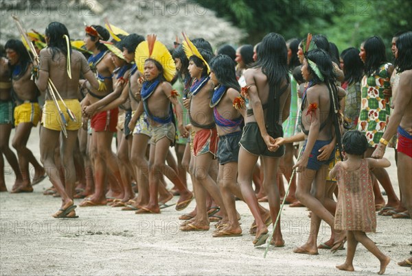 BRAZIL, Amazonas, People, Group of Xikrin Indians wearing feather head dresses and bead jewellery and with their feet and faces painted with red urucu juice.