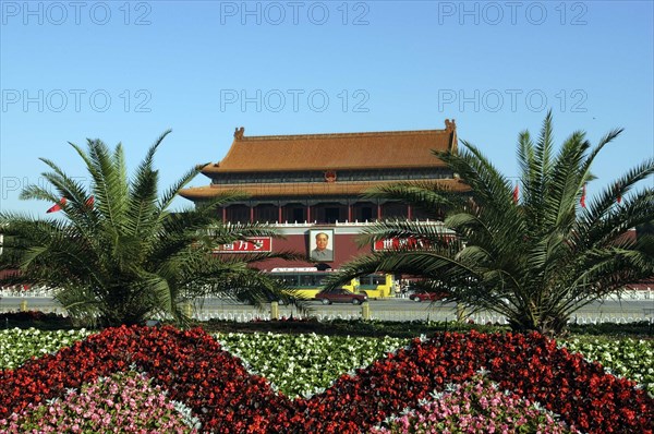 CHINA, Beijing, Tiananmen Square, Gate of Heavenly Peace or Tiananmen. View over flowerbeds and palms toward the gate building facade with large portrait of Mao