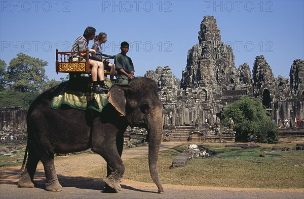 CAMBODIA, Siem Reap, Angkor Thom, Bayon Temple south facade with tourists on an elephant walking past