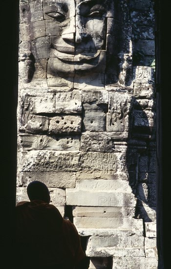 CAMBODIA, Siem Reap, Angkor Thom, Bayon Temple with a monk sitting in a doorway in front of one of the four faced towers