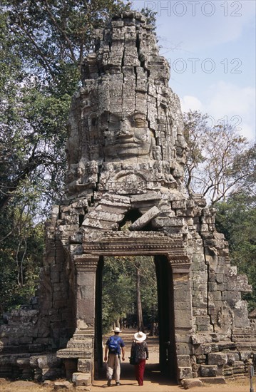 CAMBODIA, Siem Reap, Angkor, Ta Prohm monastic complex with tourists walking through the four faced west gate