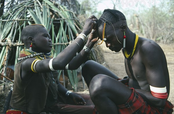 UGANDA, Karamoja, Tribal Peoples, Karamojong warrior having beaded head dress fixed by a friend.  Great pride is taken in appearance.