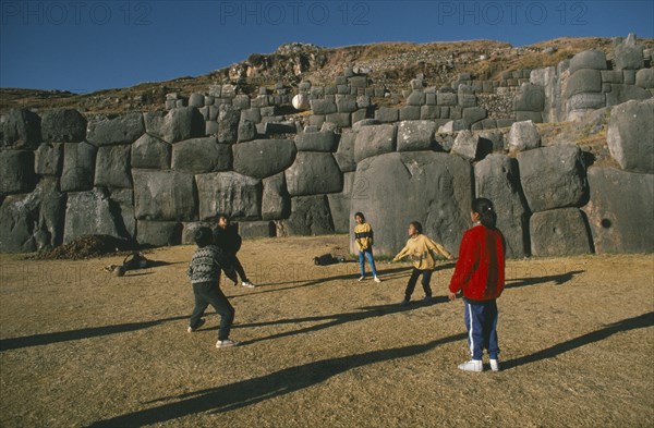 PERU, Cusco, Sacsayhuaman, Local children playing volleyball in front of walls of Inca fort on Sunday.