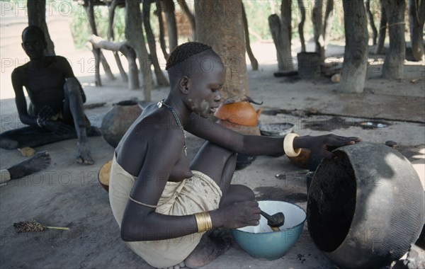SUDAN, Tribal People, Young Dinka woman ladelling the oil produced from shea butter fruit after roasting and boiling which is used for cooking and body decoration.