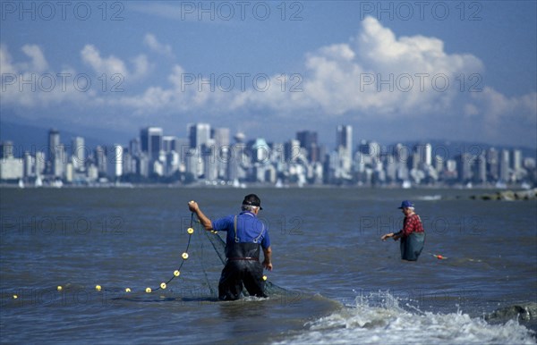 CANADA, British Columbia, Vancouver, English Bay.  Fishermen with net in foreground and skyline of downtown Vancouver beyond.