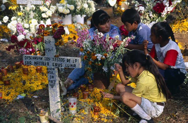 MEXICO, Michoacan, Patzcuaro, Tzurumutaro Cemetery.  Woman and children making graveside vigil as part of Day of the Dead celebrations.