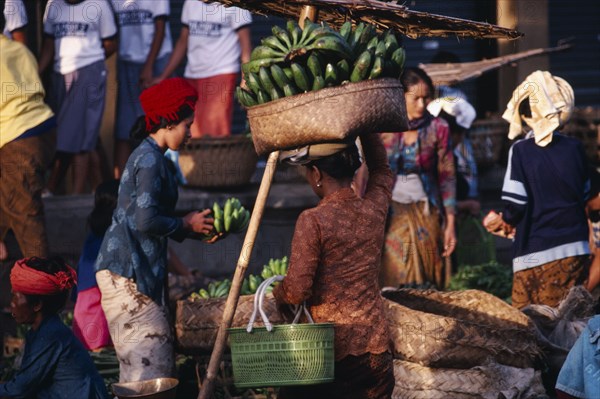 INDONESIA, Bali, Ubud, Early morning market.  Woman carrying large basket of green bananas on her head.