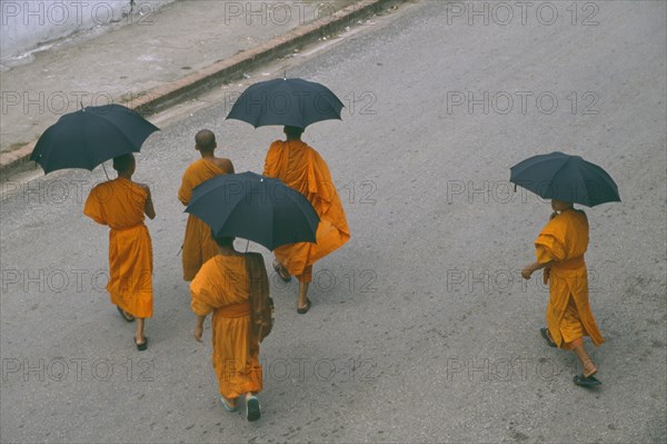 LAOS, Luang Prabang, Looking down on group of Buddhist monks carrying black umbrellas crossing street.