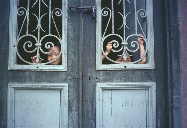 VIETNAM, North, Hanoi, Children looking out from behind decorative ironwork door panels of house in the old French Quarter.