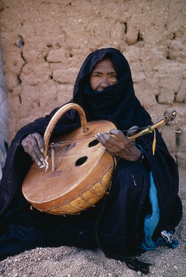 NIGER, Tribal Music, Tuareg woman playing an Imzad.  Traditional instrument consisting of a goatskin covered gourd or wooden resonator played with a curved bow and horsehair string.