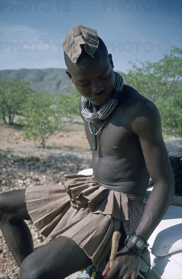 NAMIBIA, Skeleton Coast, Hoarusib Valley, Kaokoland.  Himba man sitting on bumper of safari jeep.  Cloth covering head denotes that he is married.