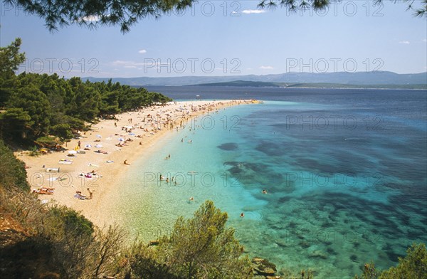 CROATIA, Brac Island, Bol, View over Zlatni Rat Beach lined with trees and scattered bathers