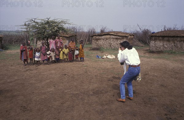 KENYA, , A Japanese tourist photographs a maasai family in a cultural manyatta set up to interface the maasai directly with tourists.