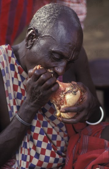 KENYA, , A maasai elder bites into a large beef bone during an initiation ceremony  which brings the Maasai Moran or young warriors into manhood. The Maasai diet consists almost entirely of meat blood and milk.