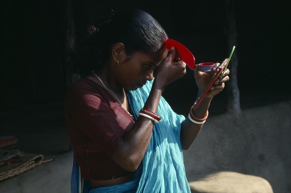INDIA, Religion, Hinduism, Young woman applying red sindoor paste to central parting of hair to signify that she is a married Hindu.