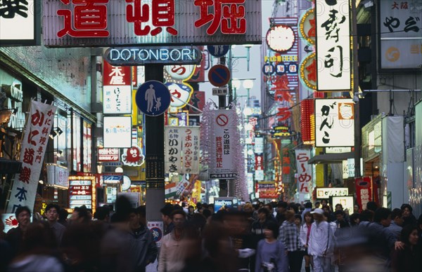 JAPAN, Honshu, Osaka, Dotonbori sign illuminated at dusk among mass of other neon signs with crowds of shoppers below