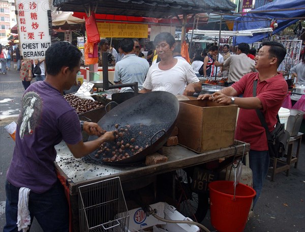 MALAYSIA, Kuala Lumpur, Chinatown, Market stall selling hot snacks cooked in a large wok with vendor and customers