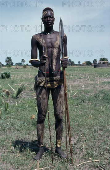 SUDAN, People, Portrait of Dinka warrior carrying spears with his body painted with a mixture of dung and ash and wearing traditional jewellery.