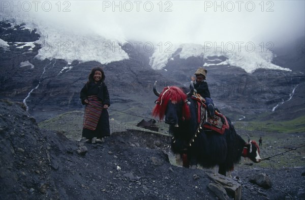 TIBET, Karo La Glacier, Nomadic children with yak in traditional decorative harness in mountain landscape.