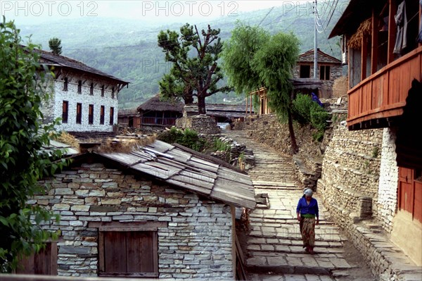 NEPAL, Ghorapani Village, View of the village with woman walking down a cobbled street