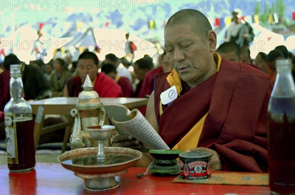 INDIA, Ladakh, Monk sitting at a table reading at the 14th Dalai Lamas birthday celebrations